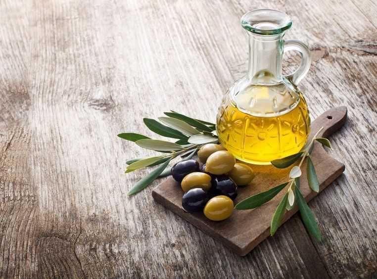 Una botella de aceite de oliva y aceitunas en una tabla de cortar sobre una mesa de madera.
