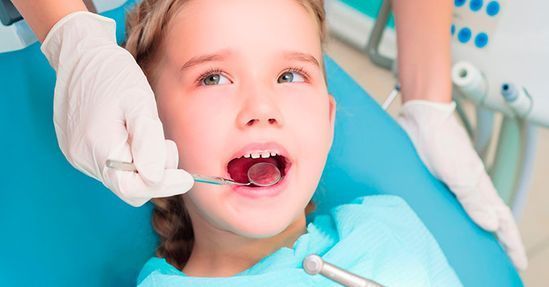 A una niña le están examinando los dientes un dentista.