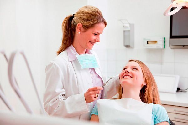 Una mujer está sentada en una silla dental hablando con un dentista.
