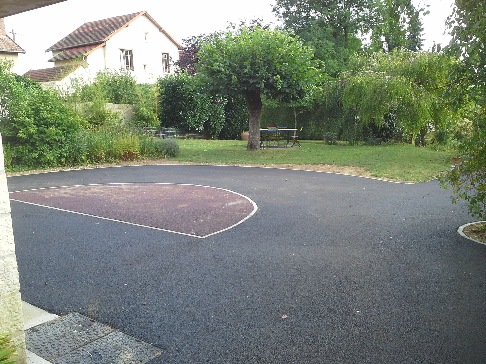 Zone d'asphalte noir avec le contour, une zone herbeuse avec un arbre et une maison en arrière-plan.