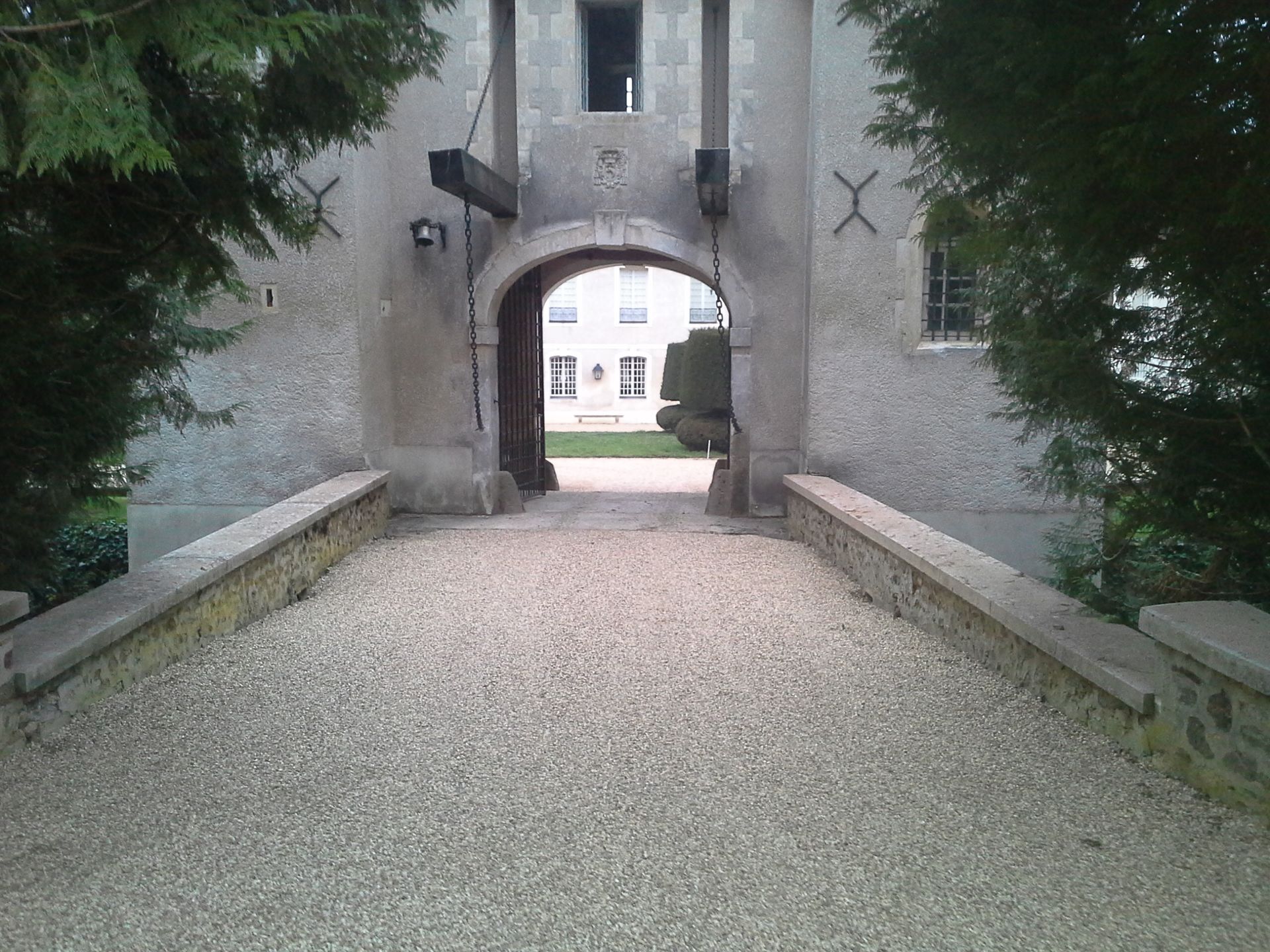 Entrée du château en pierre avec un chemin de gravier et des murs en pierre surélevés.