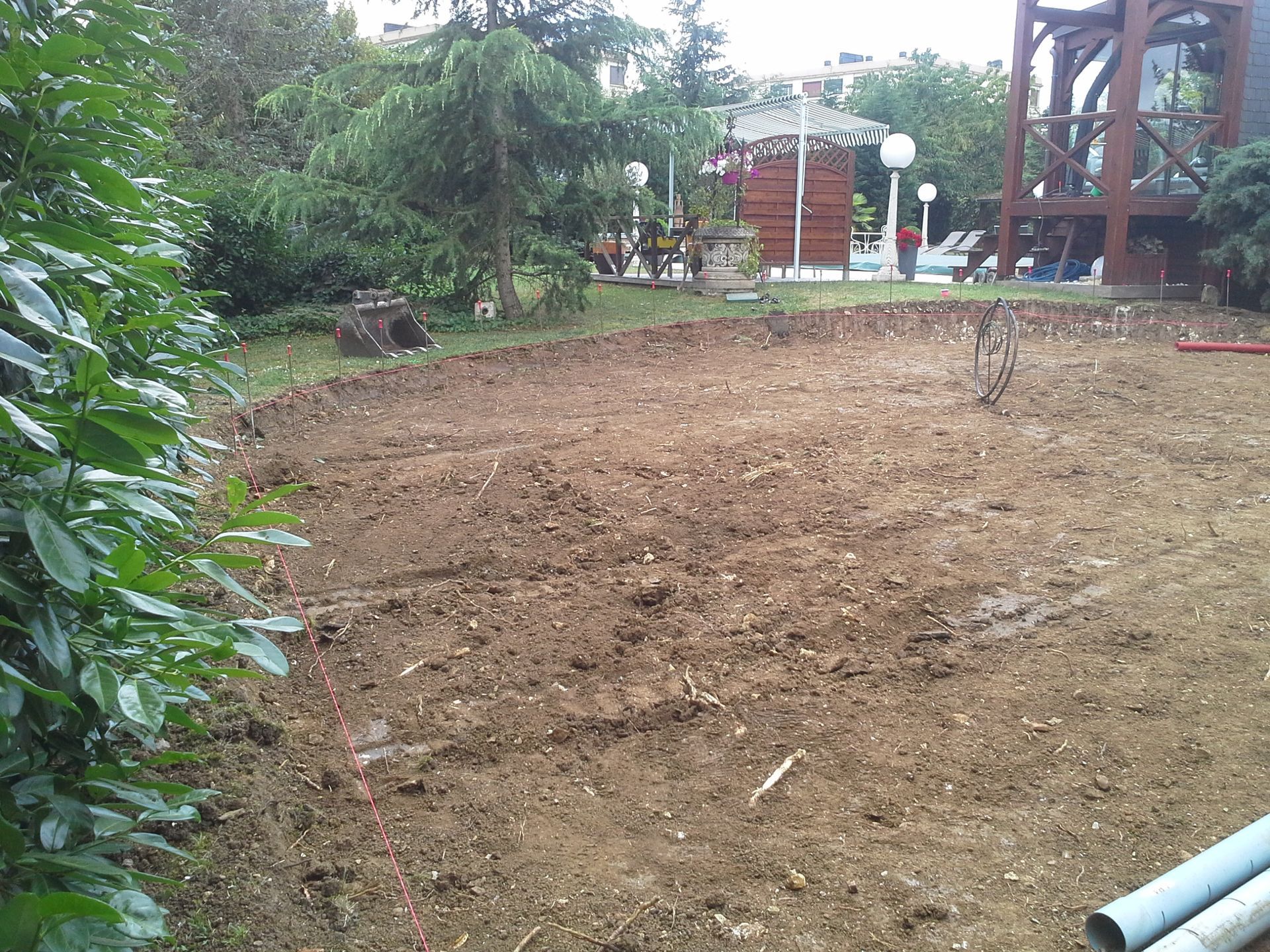 Un espace de terre nivelé dans une cour arrière, avec un petit belvédère et de la verdure en arrière-plan.