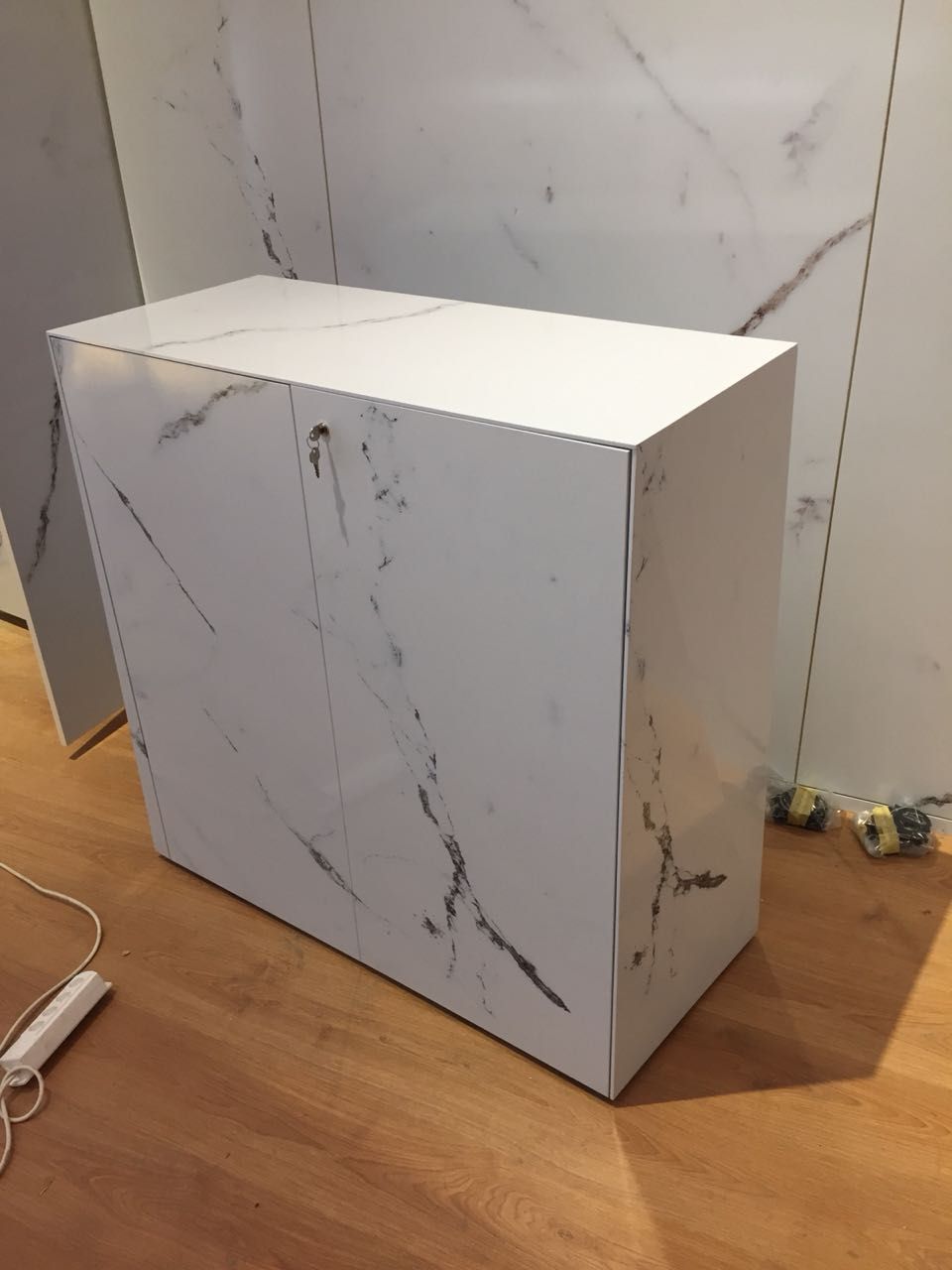 Eine weiße Kiste steht auf einem Holzboden vor einer Marmorwand.