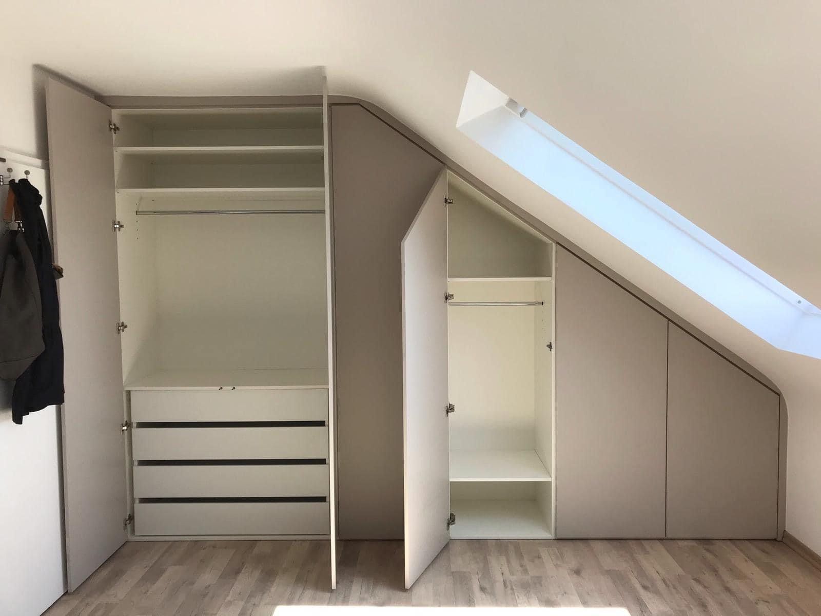 Eingebauter weißer Kleiderschrank unter der Dachschräge mit Regalen, Kleiderstange und Schubladen; eine Tür offen.