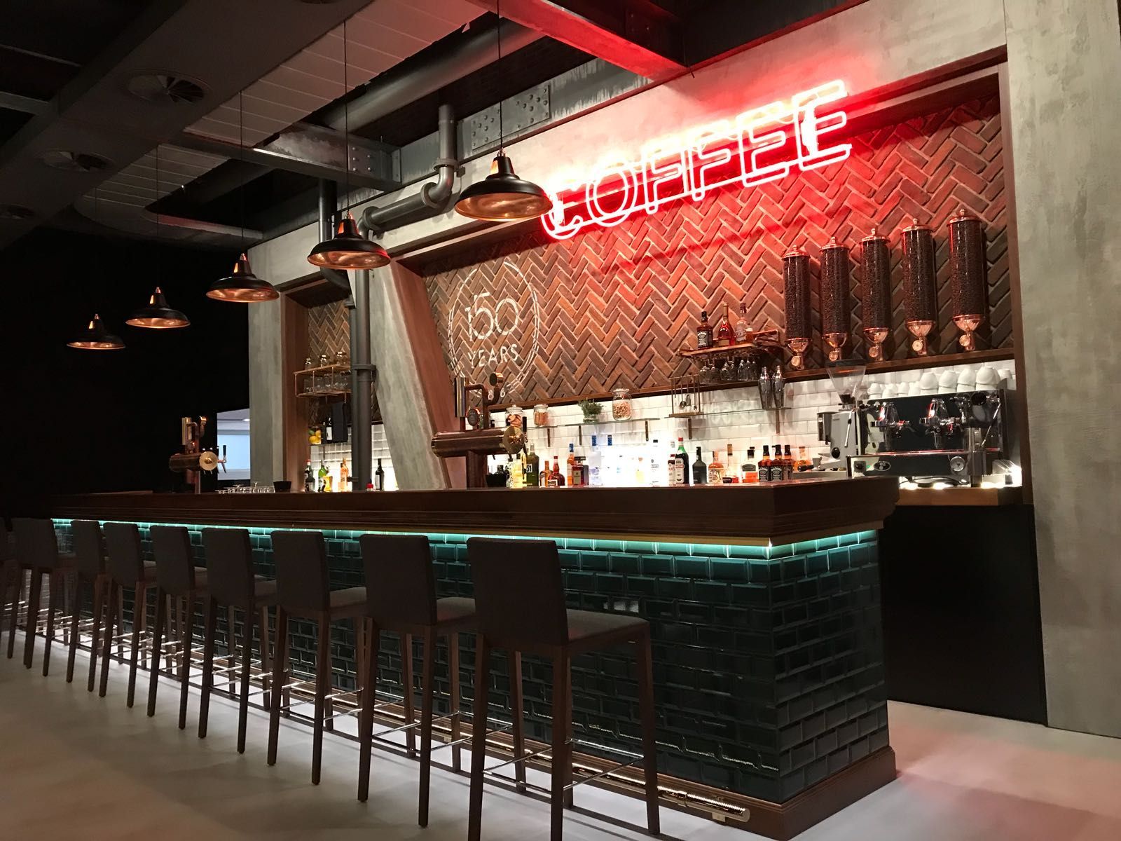 Eine lange Bar mit Hockern und einem Neonschild mit der Aufschrift „Kaffee“.