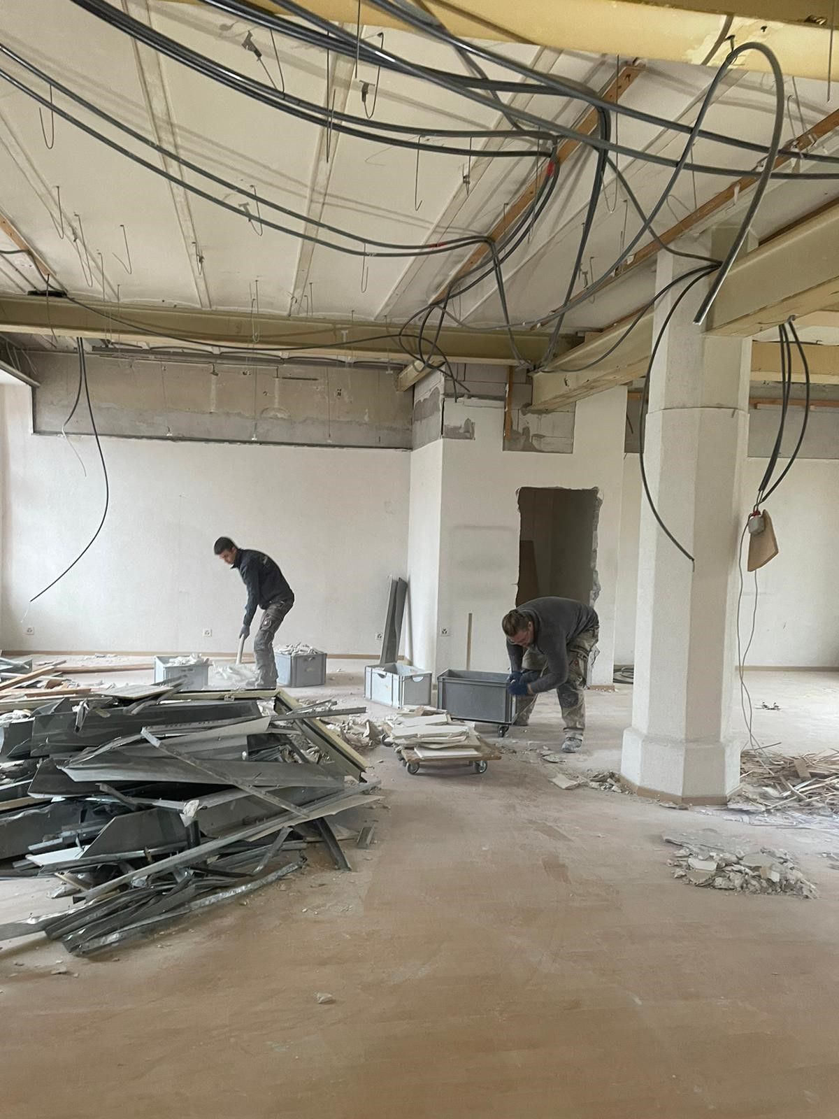 Zwei Männer arbeiten in einem großen Raum, von dessen Decke viele Kabel hängen.