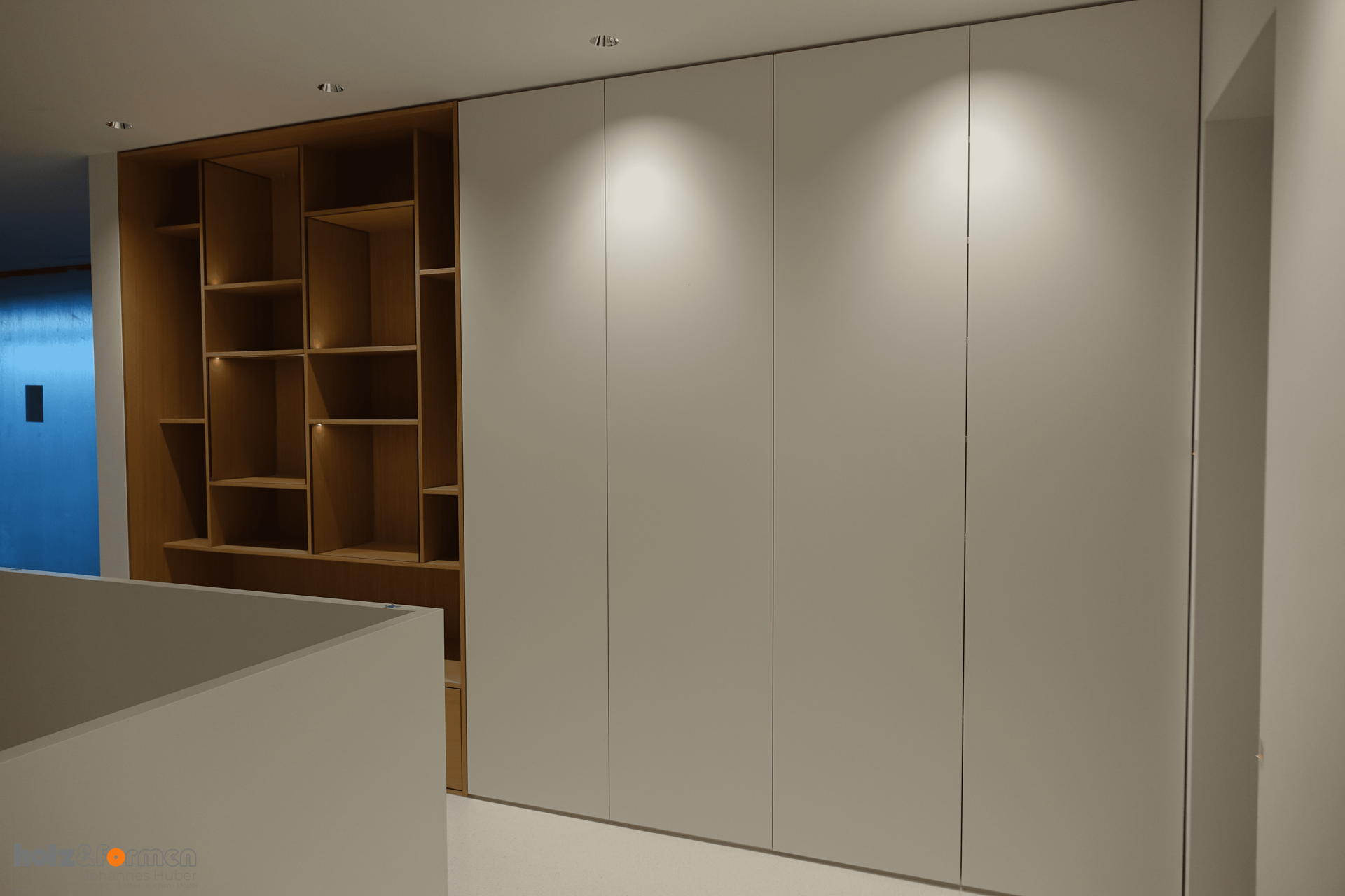 Eine große weiße Wand mit Holzregalen dahinter.