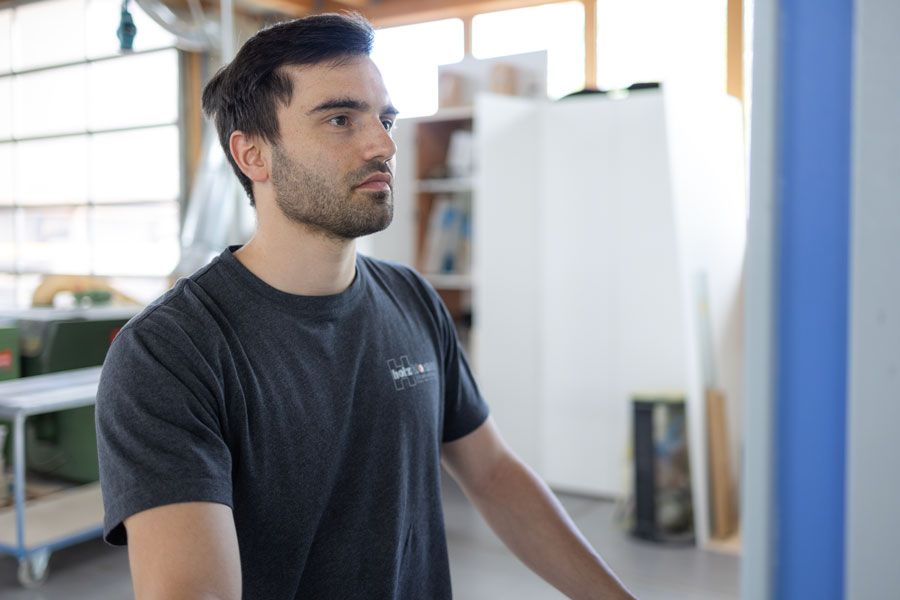 Ein Mann mit Bart steht vor einer Maschine in einer Fabrik.