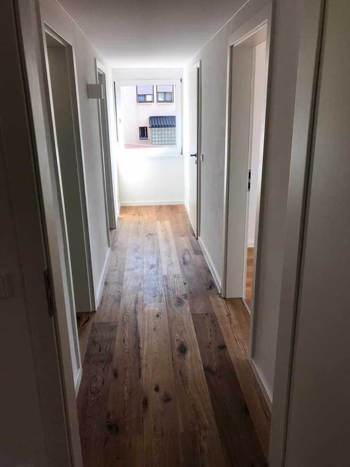 Ein langer Flur mit Holzboden und weißen Wänden.