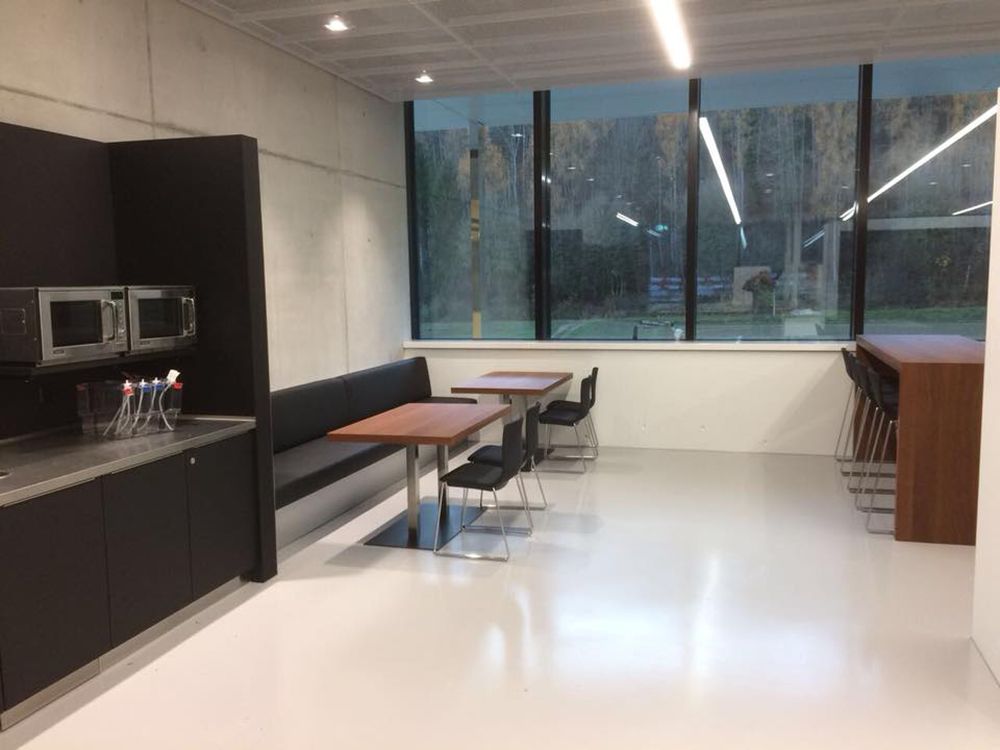 Ein Raum mit Tischen, Stühlen, einer Bank und einer Mikrowelle.