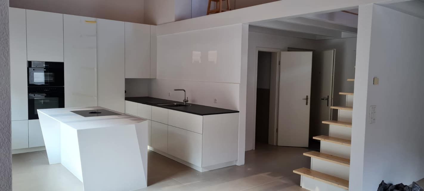 Eine Küche mit weißen Schränken, einer Spüle und einer Treppe.