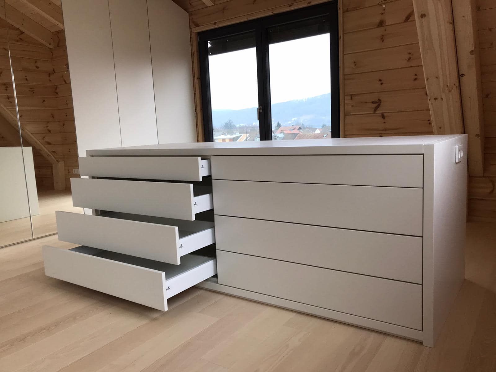 Eine weiße Kommode mit offenen Schubladen in einem Holzzimmer.