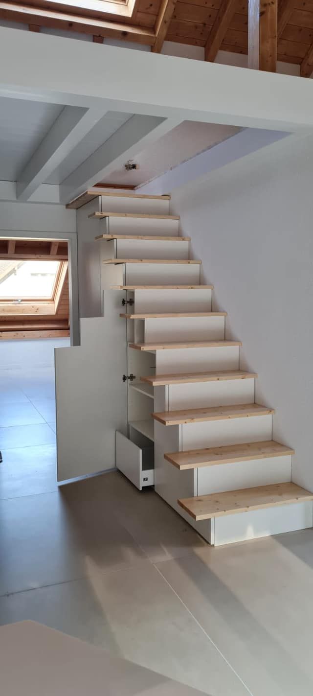 Eine weiße Treppe mit Holzstufen führt hinauf zu einem Dachboden.