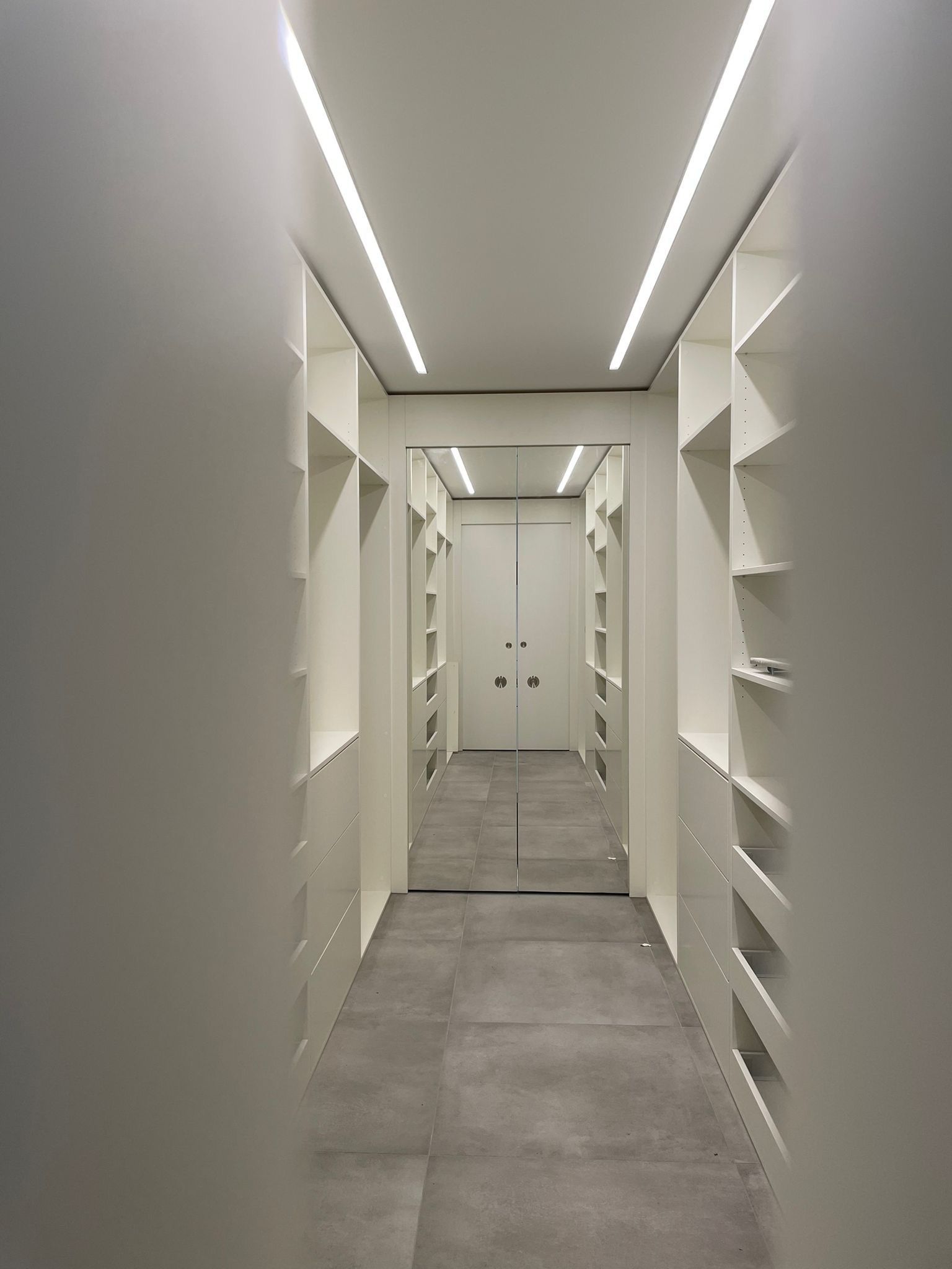 Ein langer Flur mit vielen Regalen und einem Spiegel an der Wand.