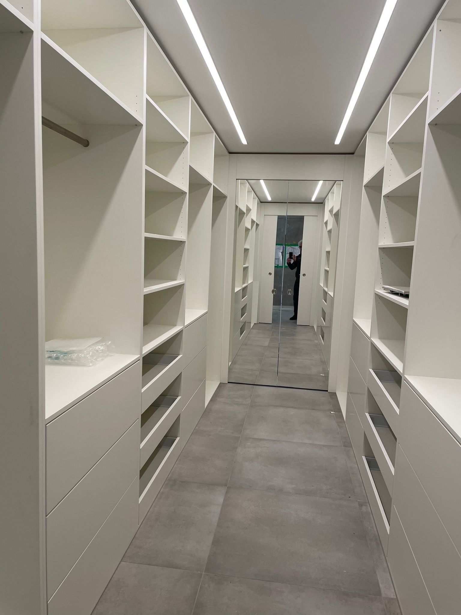 Ein sehr langer begehbarer Kleiderschrank mit vielen Regalen und Schubladen.