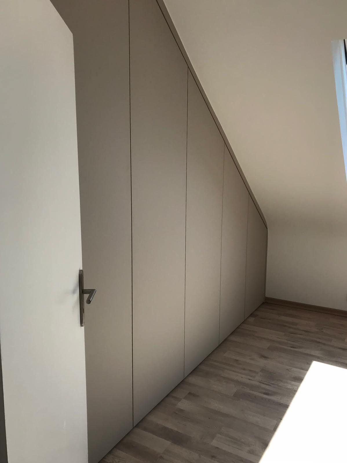 Ein Raum mit schräger Decke und einer offenen Tür.