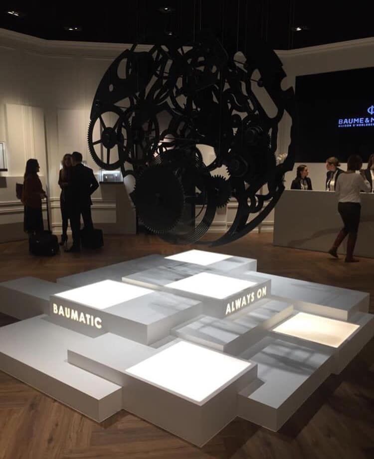 Eine Gruppe von Menschen steht um eine große Skulptur herum, auf der „Baumatic“ steht