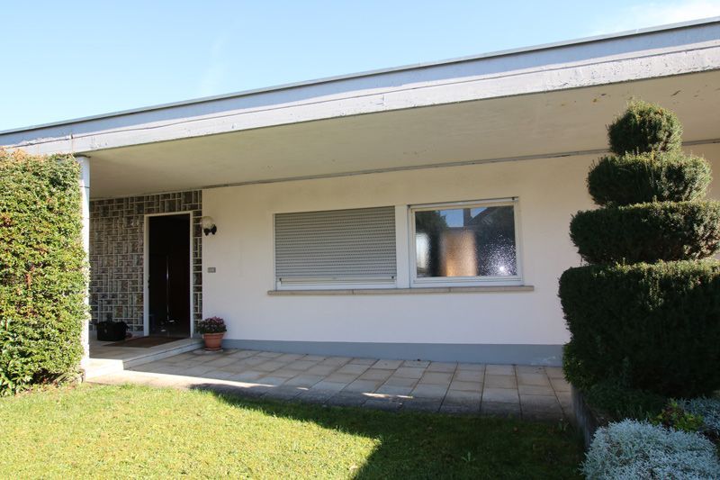 Ein weißes Haus mit einer überdachten Veranda und einem Baum davor