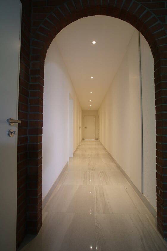Ein langer Flur mit einem gemauerten Torbogen, der zu einer Tür führt