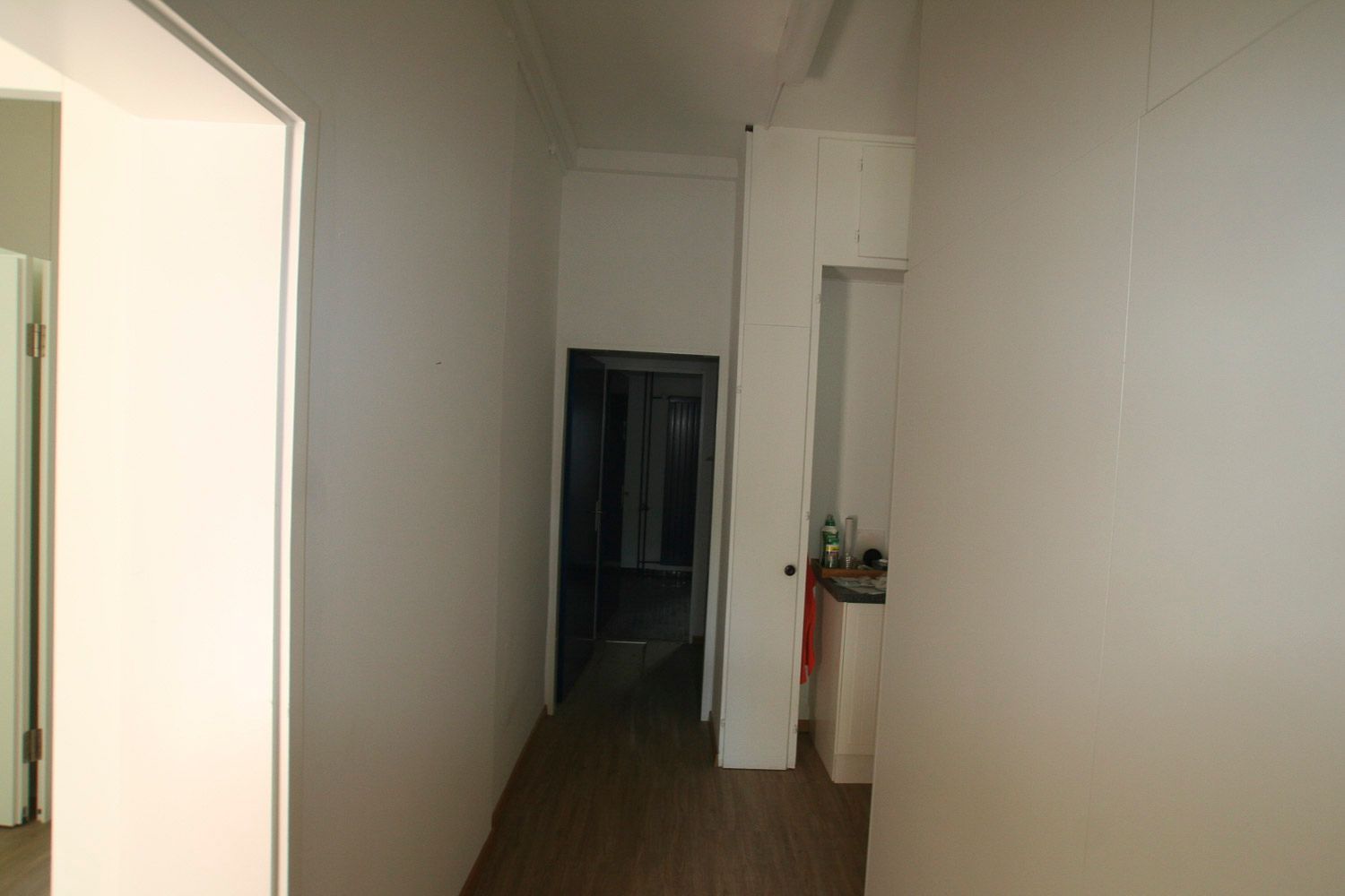 Ein langer Flur mit weißen Wänden und Holzböden in einem Haus.