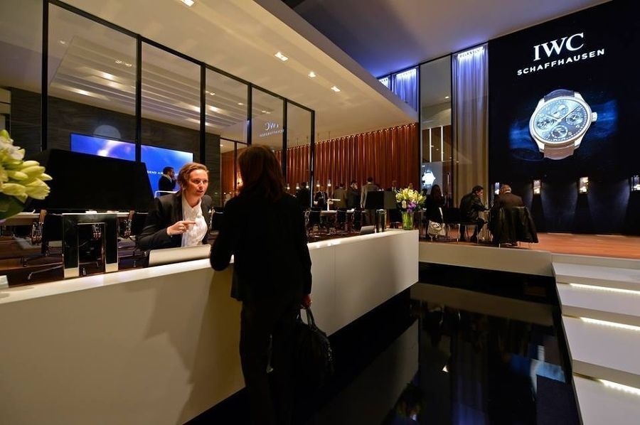 Eine Frau steht an einem Tresen vor einem Schild mit der Aufschrift „IWC“