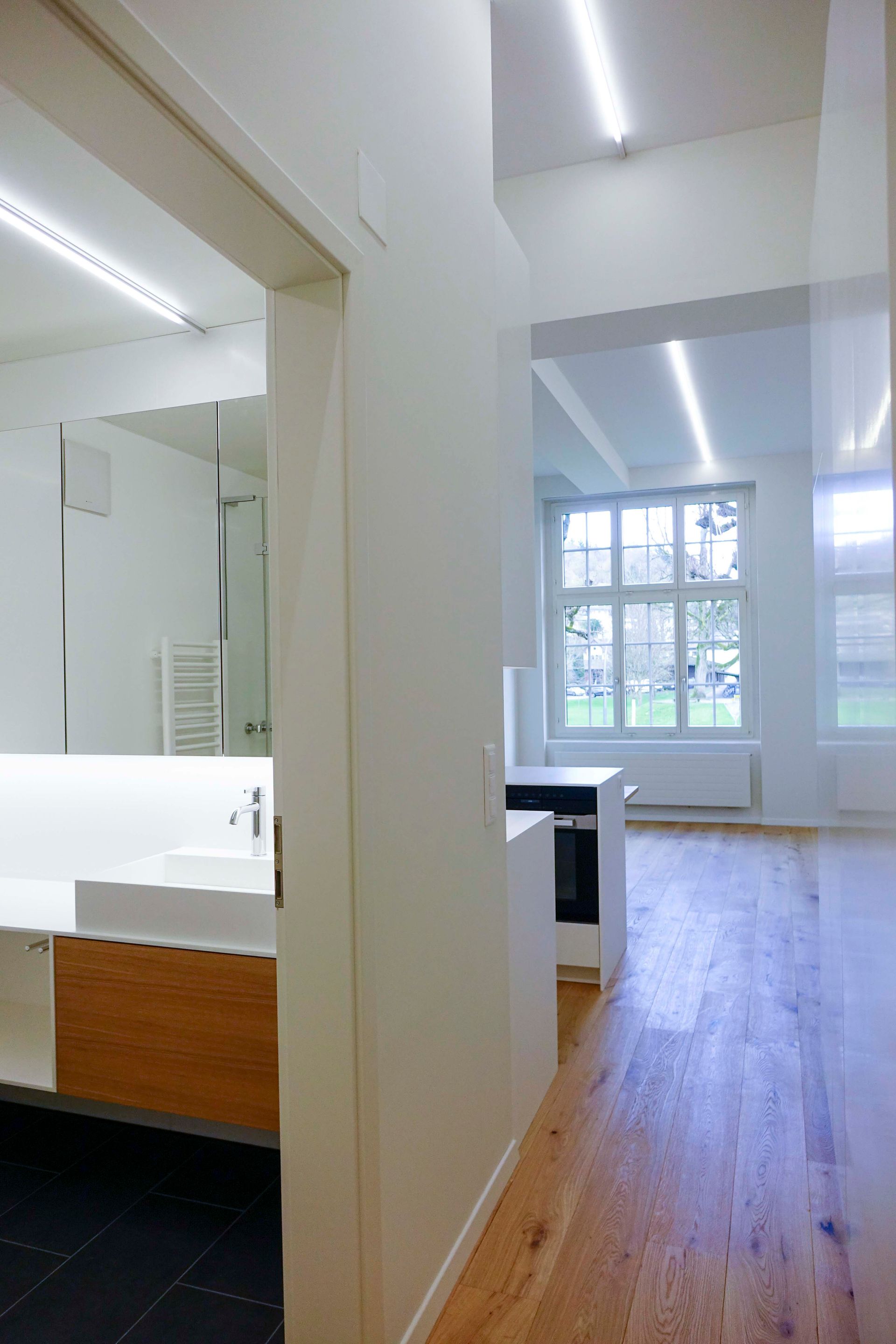 Ein Flur, der zu einem Badezimmer mit Waschbecken und Spiegel führt.