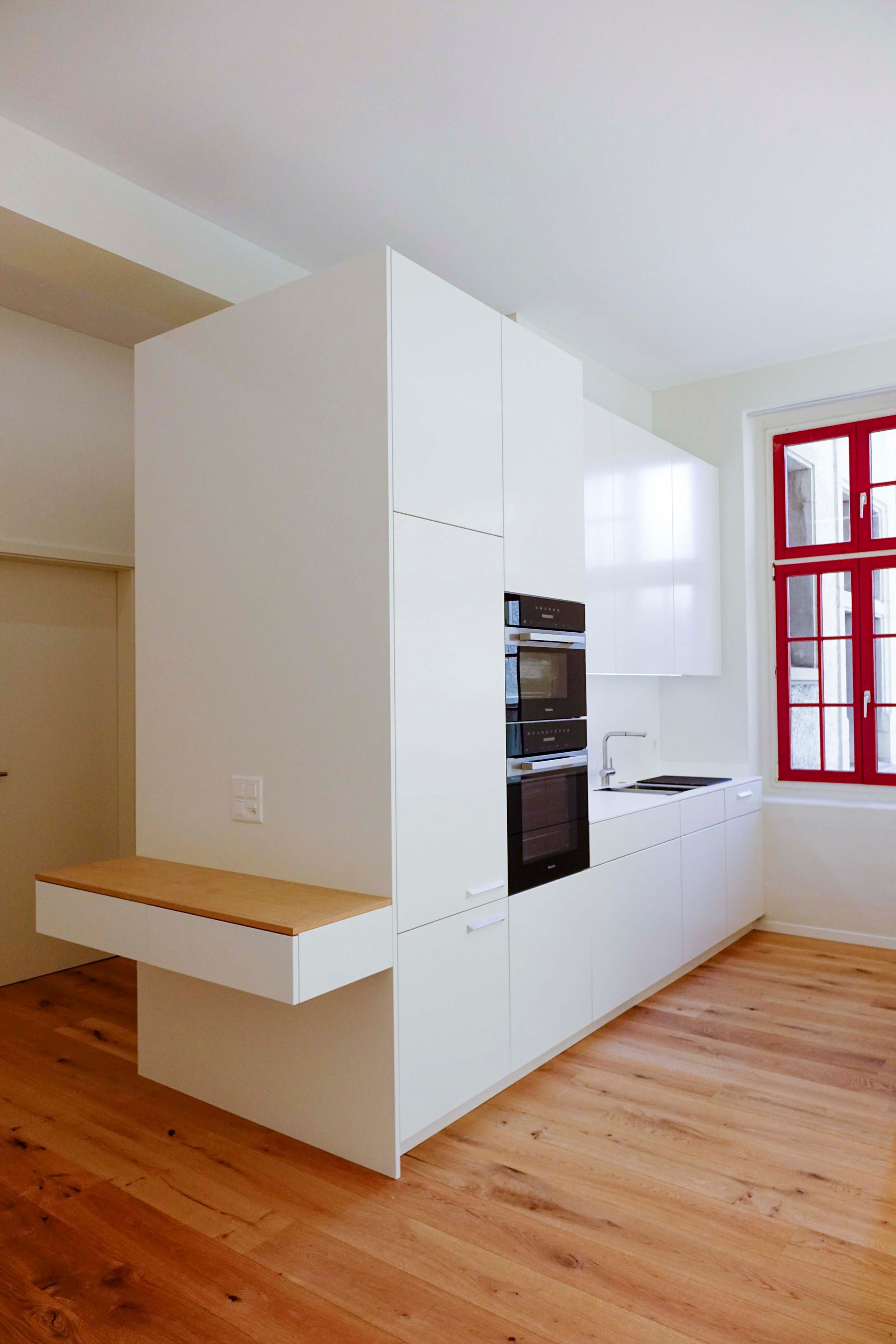 Eine Küche mit weißen Schränken und Holzböden und einem roten Fenster.