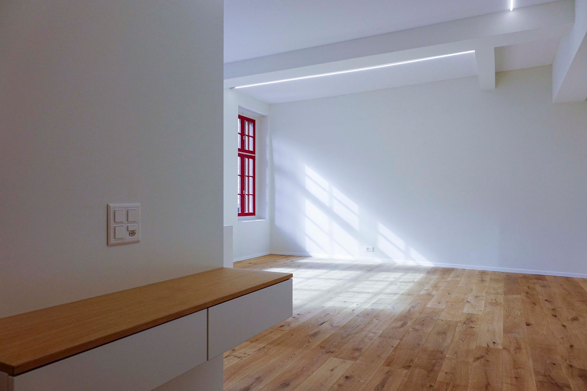 Ein leerer Raum mit Hartholzböden und einem roten Fenster.