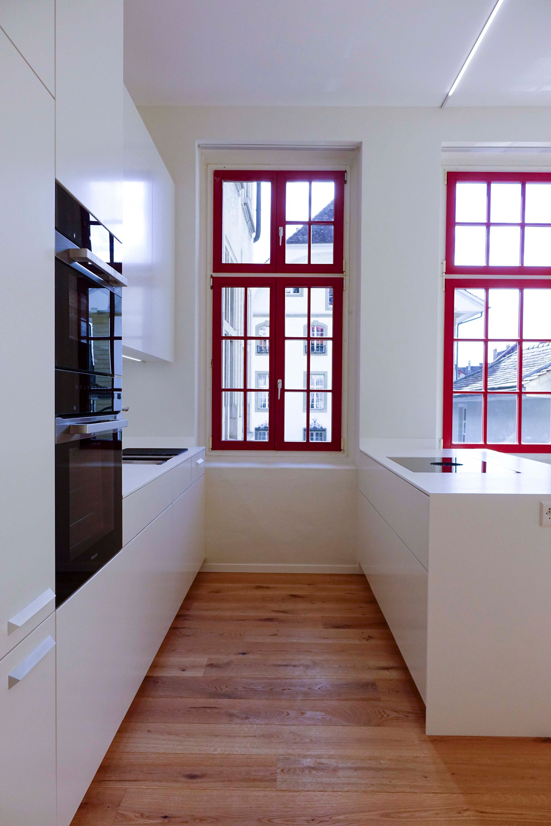 Eine Küche mit weißen Schränken, Holzböden und roten Fenstern.