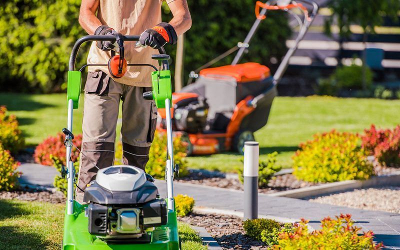 Un homme utilise une tondeuse à gazon verte pour couper l'herbe dans un jardin.