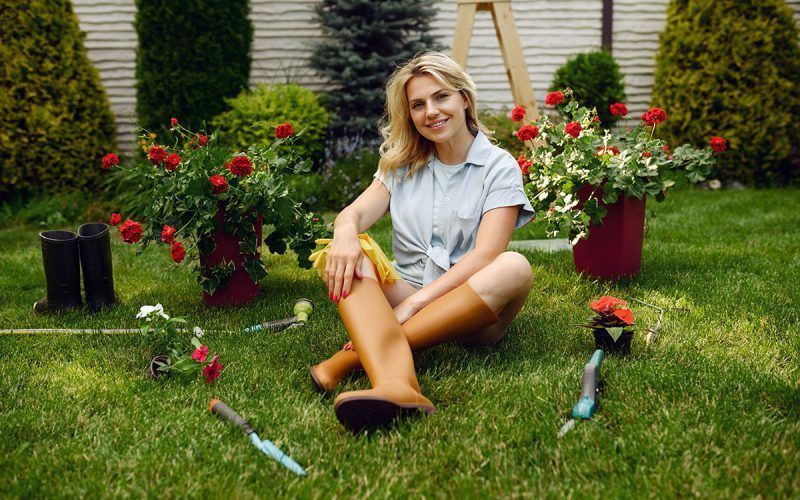 Une femme est assise sur l'herbe dans un jardin avec des fleurs et des outils de jardinage.