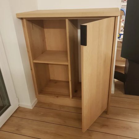 Ein heller, holzfarbener Schrank mit einem offenen Fach und einer Tür