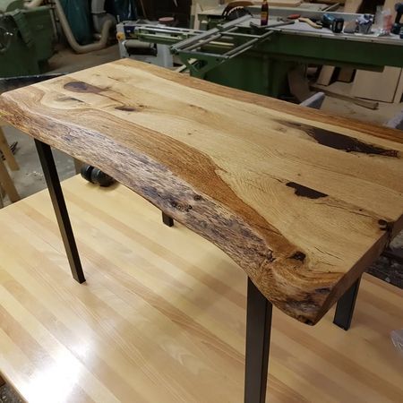 Ein Konsolentisch aus Massivholz mit natürlicher Maserung und dunklen Metallbeinen steht in einer Werkstatt.