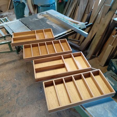 Vier hölzerne Schubladeneinsätze mit unterschiedlicher Fächeraufteilung stehen auf einem Werkstatttisch.