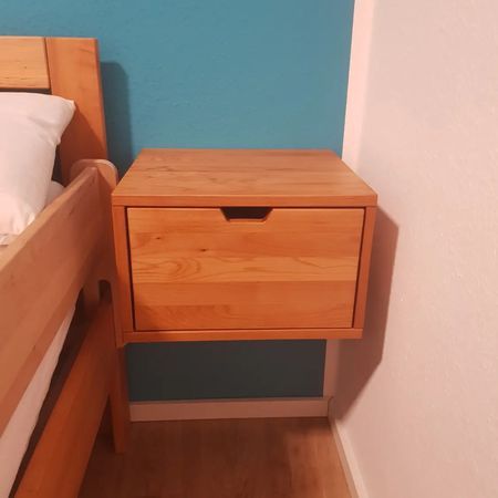 Ein schwebender Nachttisch aus hellem Holz mit einer einzelnen Schublade