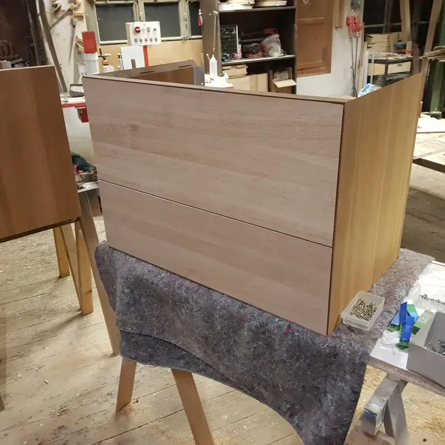 Auf einer Werkbank in einer Holzwerkstatt steht ein unfertiger Holzschrankrahmen.