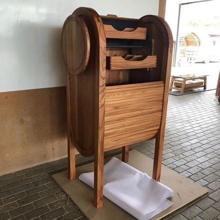 Ein hoher Holzschrank mit Rolltür, Innenregalen und kreisförmigem Seitendesign in einer Werkstatt.