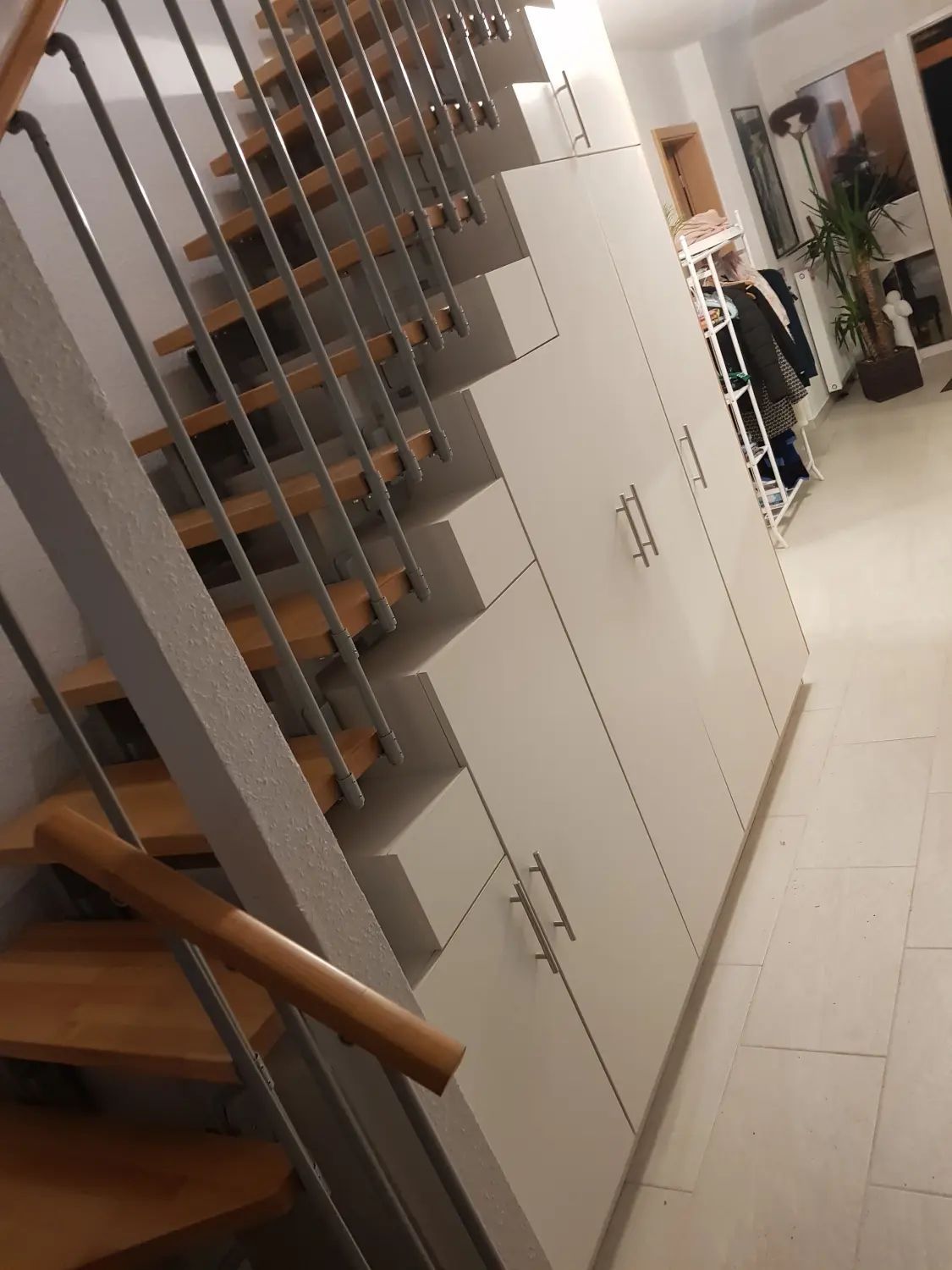 Eine Holztreppe mit Metallgeländer neben einem maßgefertigten, weißen, mehrstufigen Aufbewahrungsschrank