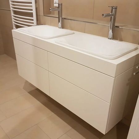 Ein moderner, weißer Doppelwaschtisch mit Chromarmaturen, montiert an einer gefliesten Badezimmerwand.