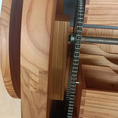 Nahaufnahme einer Holzkonstruktion mit keilgezinkten Paneelen und einem Metallkettenmechanismus auf einer zentralen Achse.