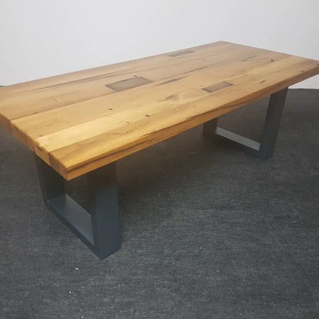 Ein rechteckiger Esstisch aus Holz mit natürlicher Kante und dunkelgrauen, U-förmigen Metallbeinen