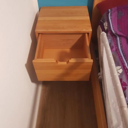 Ein schwebender Nachttisch aus hellem Holz mit offener Schublade