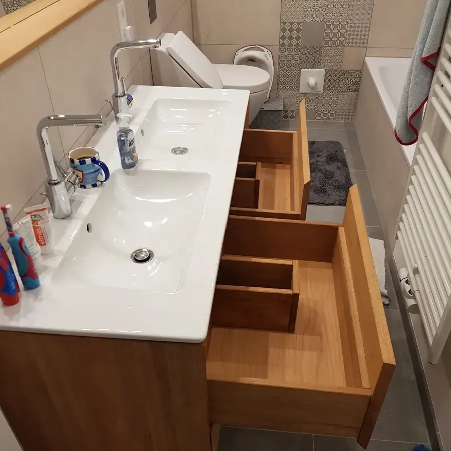 Ein Badezimmerschrank mit zwei Waschbecken und geöffneten Holzschubladen, daneben Toilette, Badewanne und Handtuchhalter.