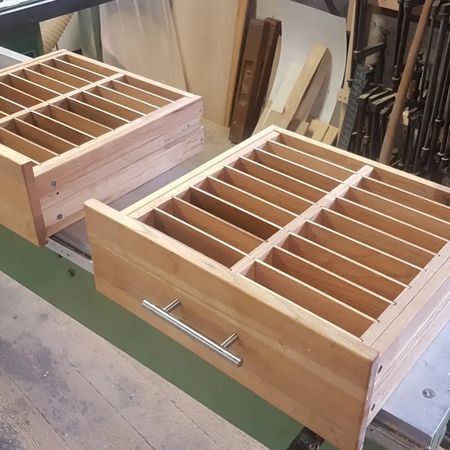 Zwei unfertige Holzschubladen mit Inneneinteilungen stehen auf einer Werkbank in einer Holzwerkstatt.