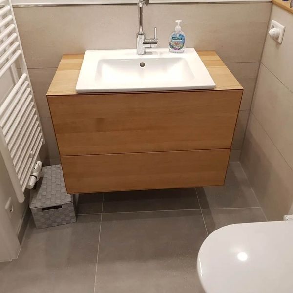 Ein an der Wand montierter Waschtisch aus hellem Holz mit weißem rechteckigem Waschbecken und Wasserhahn