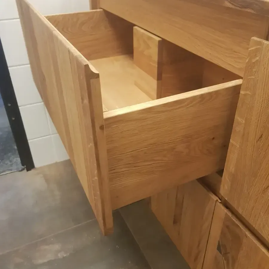 Eine offene, helle Holzschublade in einem Badezimmerschrank mit Fliesenboden.