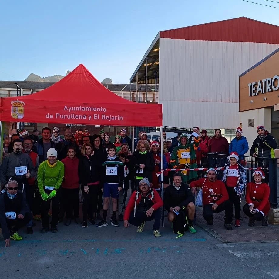 Grupo de corredores posando bajo una carpa roja, afuera de un edificio etiquetado 