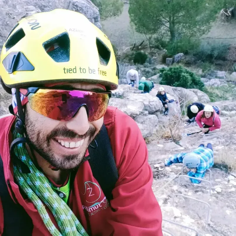 Niño y mujer escalando una pared de roca con peldaños metálicos fijos, usando cascos y chaquetas.