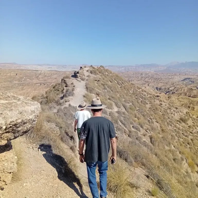 Excursionistas en un sendero con vistas a un valle bajo un cielo azul con nubes.