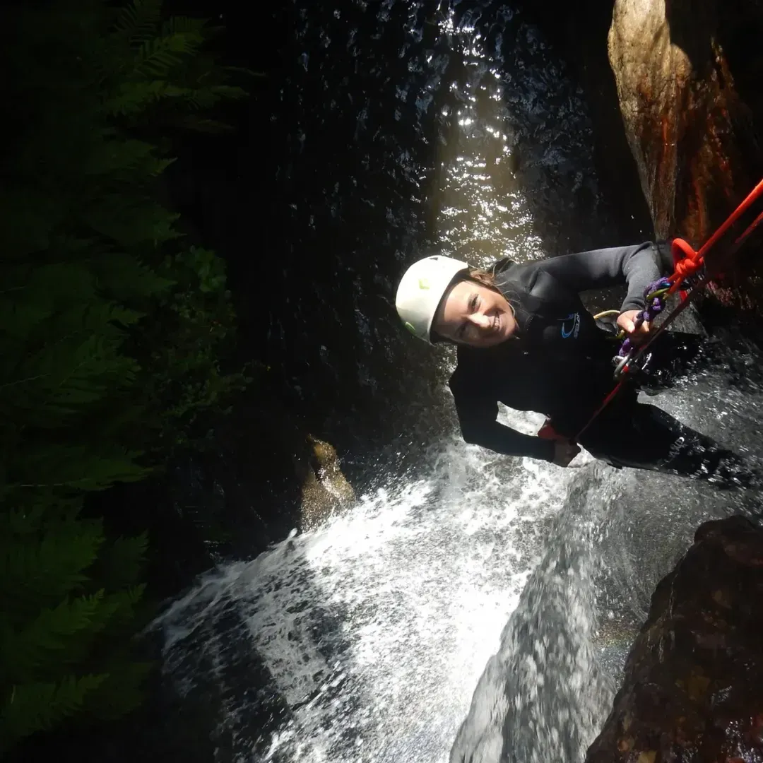 Persona haciendo rapel por una cascada en un cañón, usando casco y traje de neopreno.